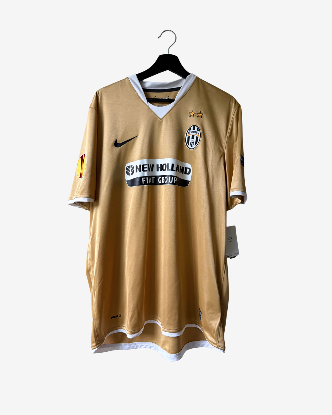 A vintage Nike Juventus home soccer jersey in gold with white trim, hanging on a black hanger against a light gray background. The jersey features the black Nike swoosh, the Juventus crest, and the New Holland sponsor logo.