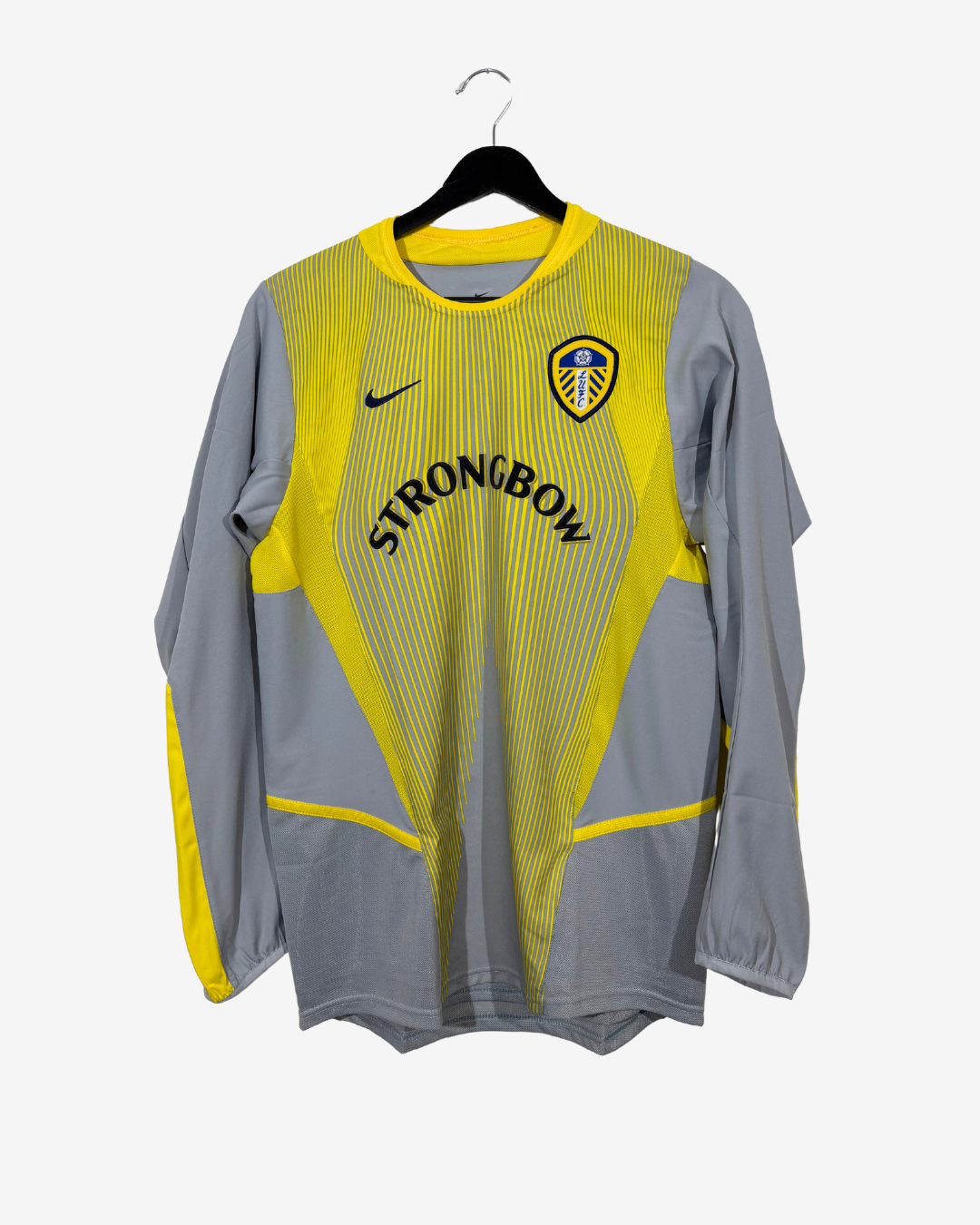A Nike long-sleeve soccer jersey in gray and yellow, hanging on a black hanger against a light gray background. The jersey features the Leeds United crest, a black Nike swoosh, and 'STRONGBOW' printed across the chest.