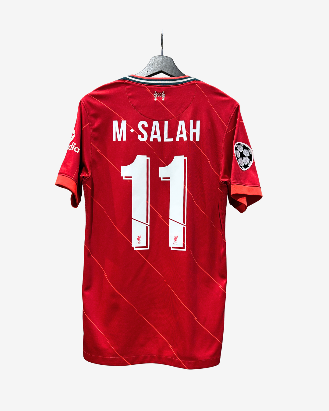 A red short-sleeve soccer jersey hanging on a hanger against a light gray background, showing the back with 'M-SALAH' and the number '11' in white. The jersey has subtle diagonal stripe patterns and sleeve patches.