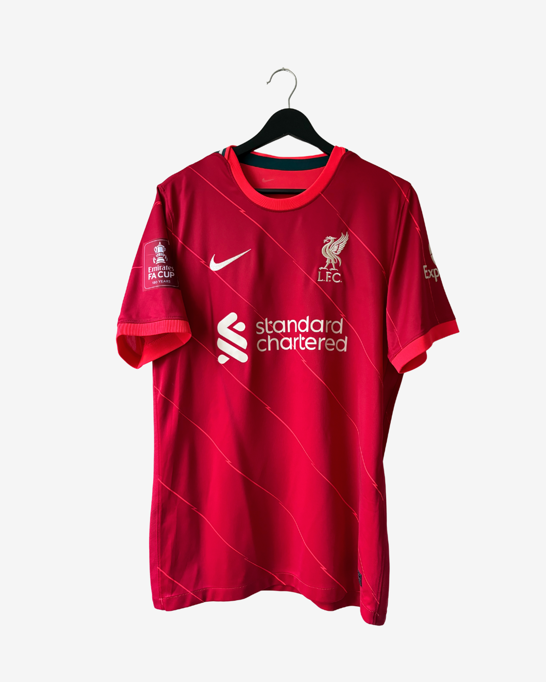 A red Liverpool FC short-sleeve soccer jersey hanging on a black hanger against a light gray background. The jersey features the white Nike swoosh, the Liverpool FC crest, the Standard Chartered sponsor logo, and a Premier League patch on the sleeve.
