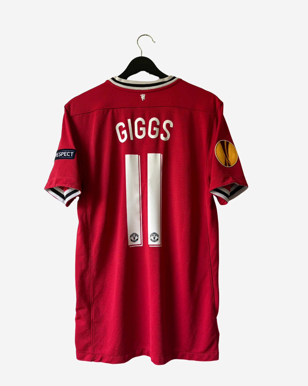 A red short-sleeve football jersey hanging on a black hanger against a light gray background. The back of the shirt shows the name 'GIGGS' in white block letters above the number '11' in white, with Manchester United crest logos near the bottom of the numbers.