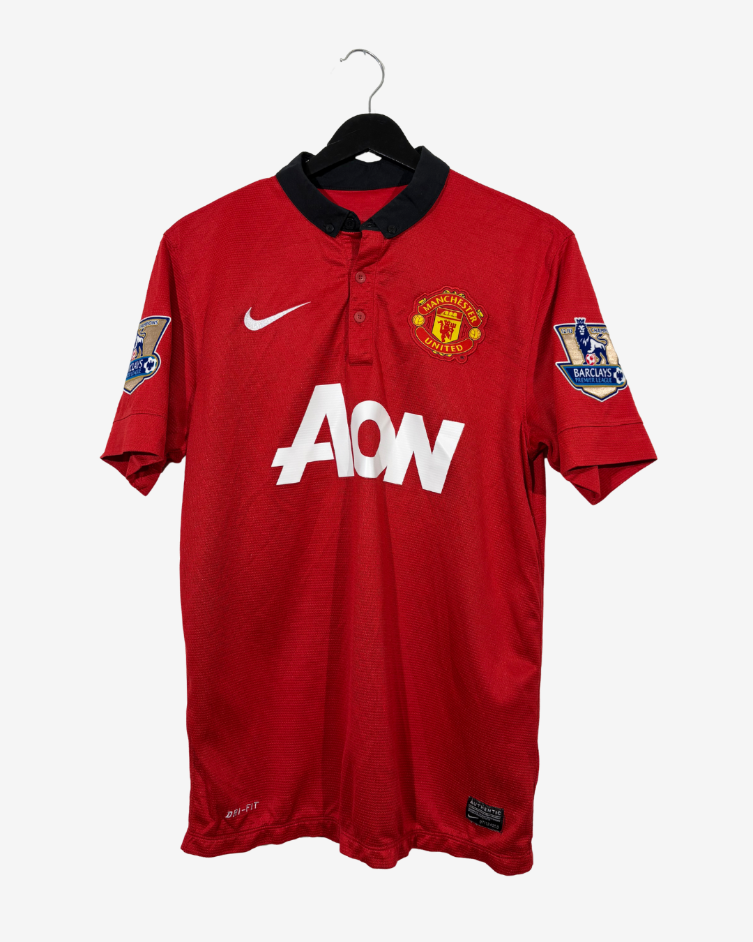 A red Manchester United short-sleeve soccer jersey with a black collar, featuring the white AON sponsor logo on the front, a white Nike swoosh, and the Manchester United crest on the left chest. The jersey is displayed on a black hanger against a light gray background.