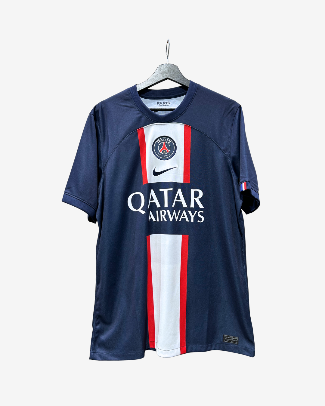 A Paris Saint-Germain Nike soccer jersey in navy blue, featuring red and white vertical stripes on the front, with the Paris Saint-Germain crest, Nike swoosh, and Qatar Airways sponsor logo.