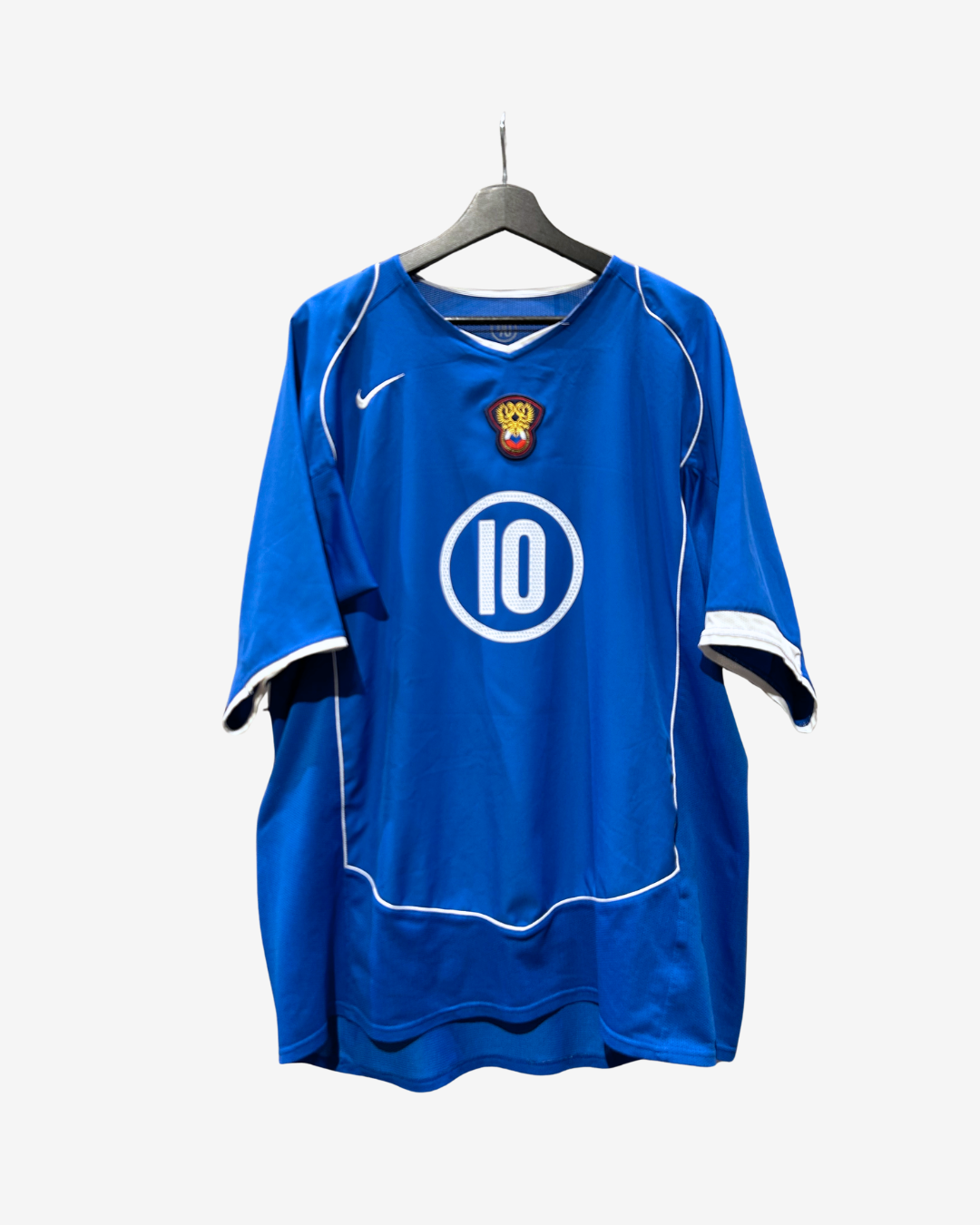 A blue short-sleeve soccer jersey hanging on a black hanger against a light gray background. The jersey features a white Nike swoosh on the right chest, a small crest with a lion and crown on the left chest, and a large white circle containing the number 10 in the center.