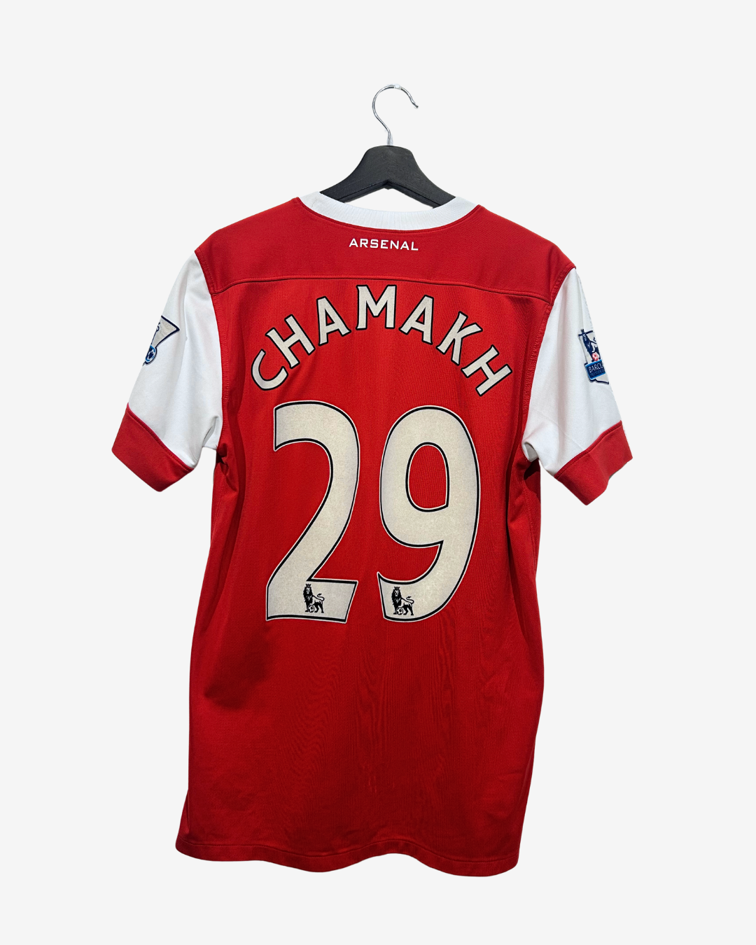 Red and white Arsenal football jersey shown from the back, hanging on a black hanger against a light gray background. The back features the name CHAMAKH and number 29 in cream lettering.