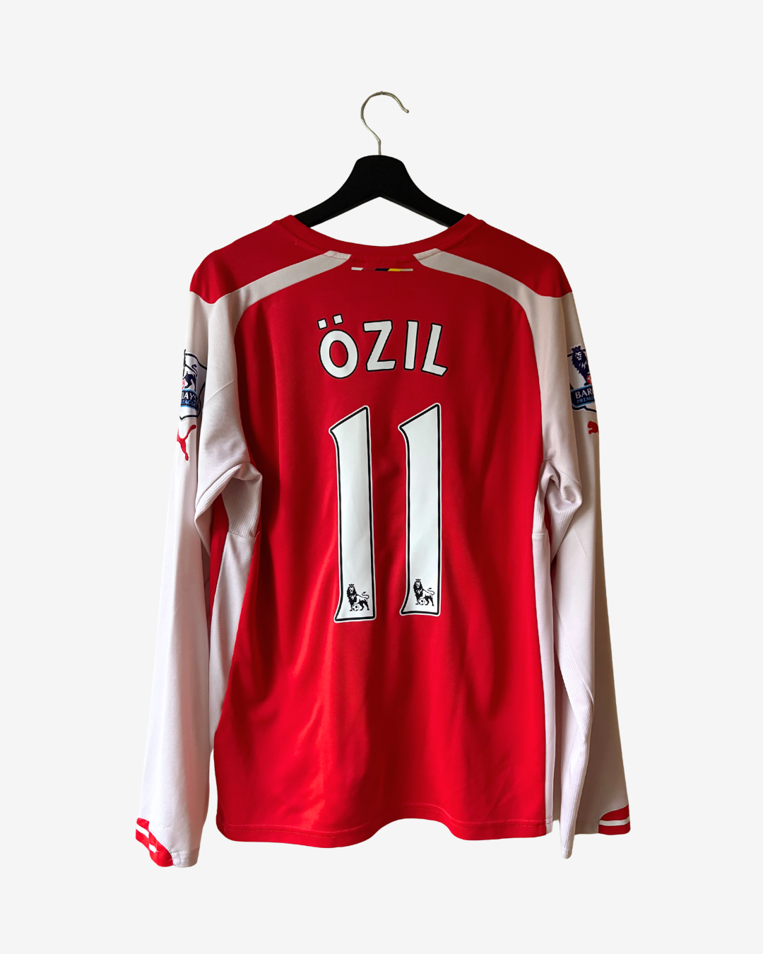 A red and white long-sleeve soccer jersey hanging on a black hanger against a light gray background. The back of the jersey features the name 'ÖZIL' and the number '11' in white with black outlines.
