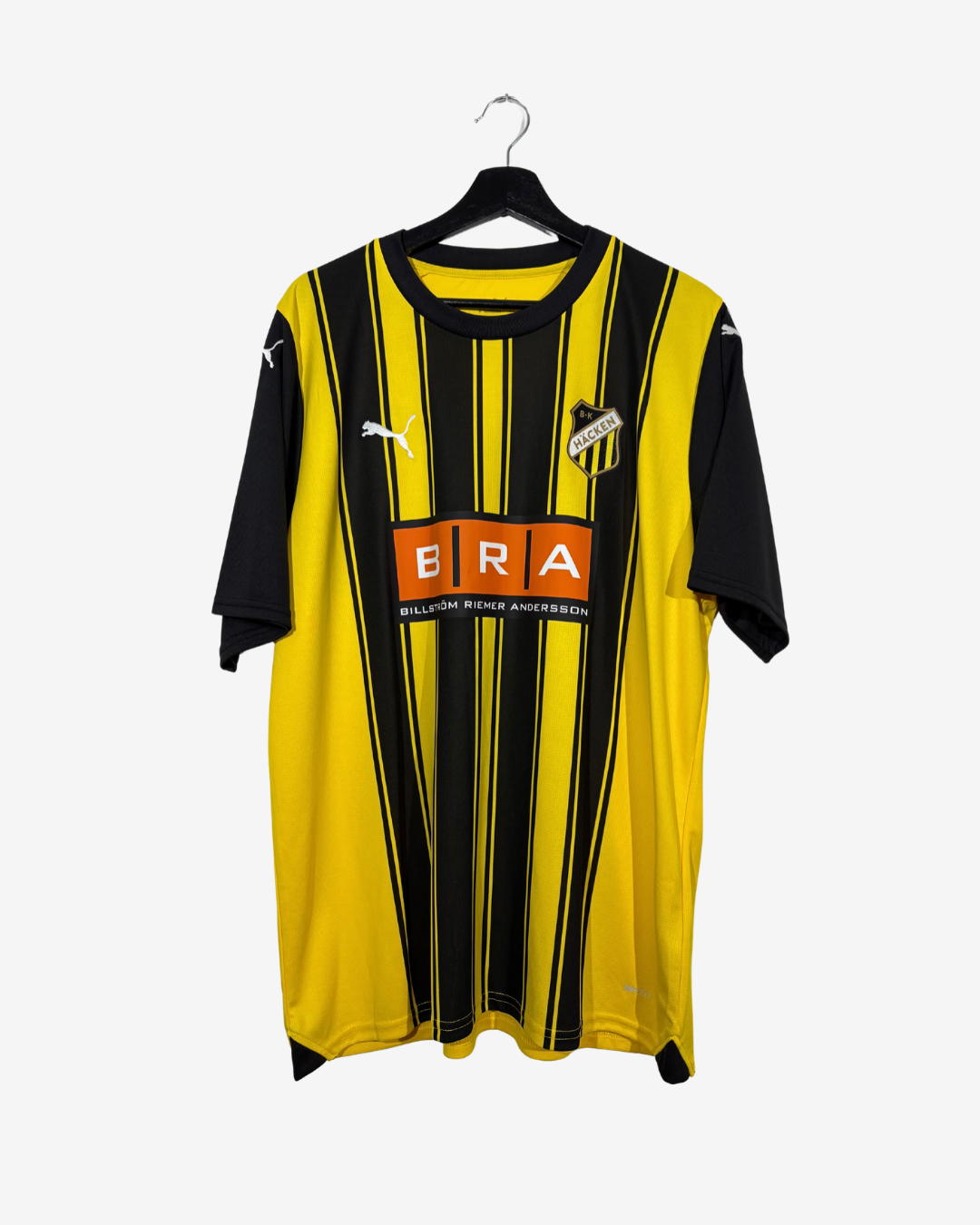 A yellow and black vertically striped Puma soccer jersey with a black collar and sleeves, featuring the bra sponsor logo on the chest, hanging on a black hanger against a light gray background.