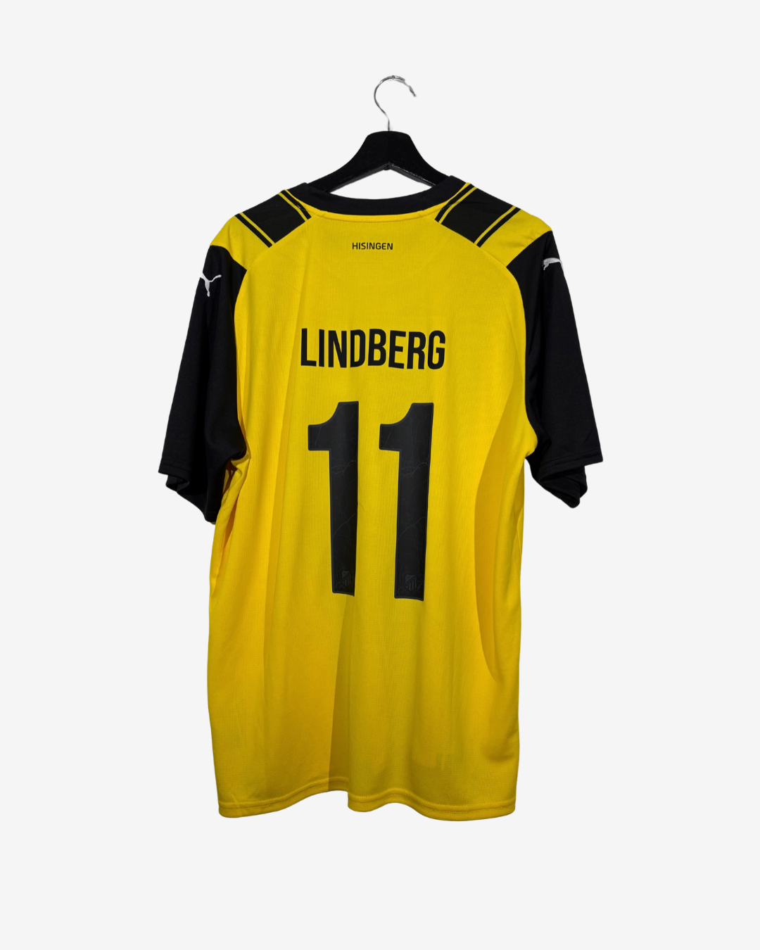 A yellow and black Puma soccer jersey with the name 'LINDBERG' and number '11' printed on the back, hanging on a black hanger against a light gray background.