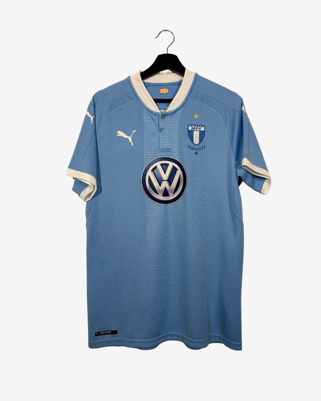 A light blue Puma soccer jersey for Malmö FF, featuring the Volkswagen logo on the center chest, a Puma logo on the right chest, and a club crest on the left chest, hanging on a black hanger against a light gray background.