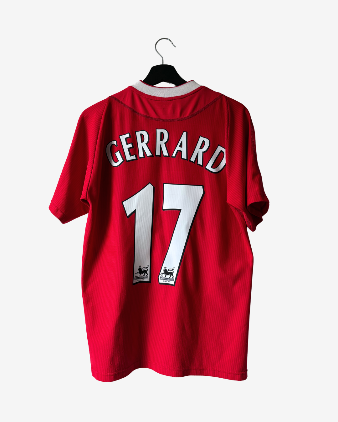 A red short-sleeve soccer jersey hanging on a black hanger against a light gray background. The back of the shirt features the name 'GERRARD' and number '17' in white with black outlines.