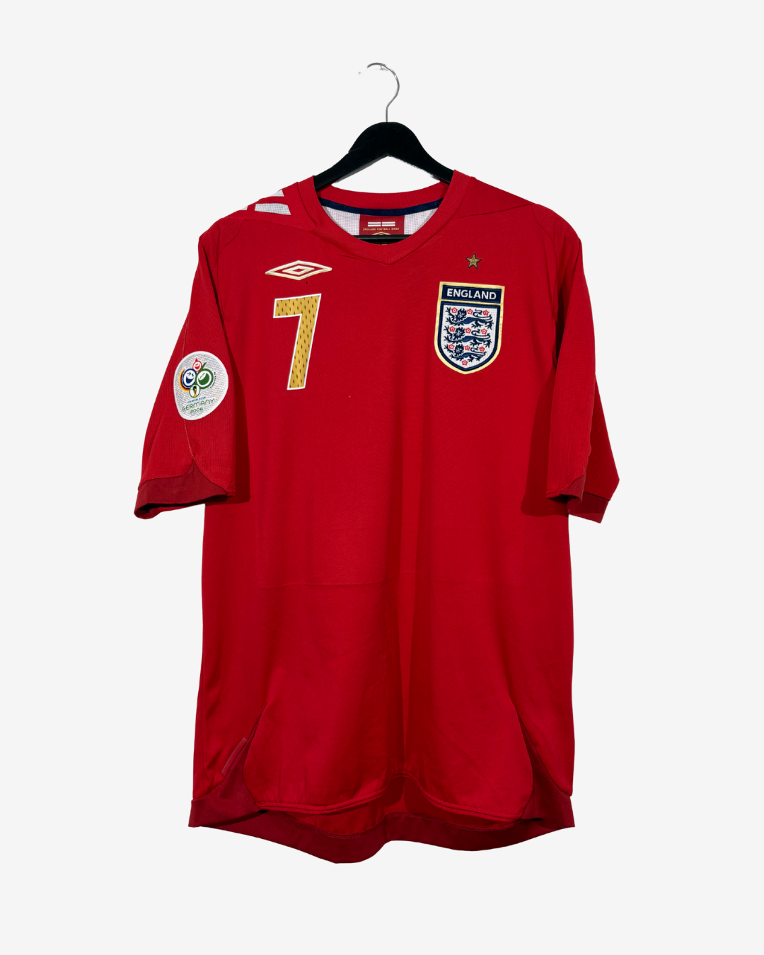 A red England national football team jersey with the number 7 on the chest, featuring the Umbro logo and England crest, hanging on a black hanger against a light gray background.