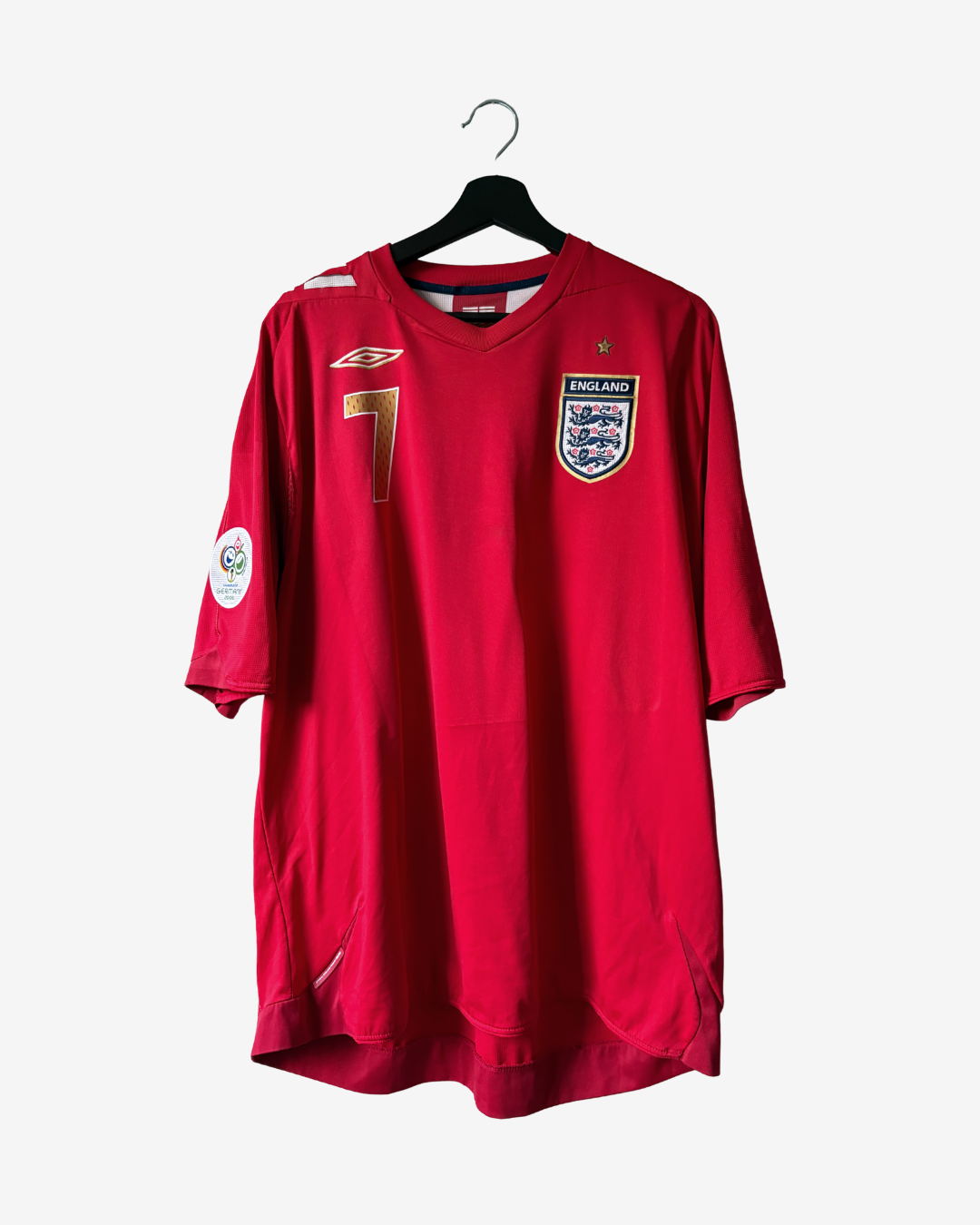 A red England national football team jersey with the number 7 on the chest, featuring the Umbro logo and England crest, hanging on a black hanger against a light gray background.