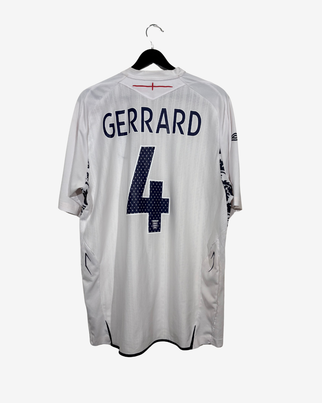 A white short-sleeve soccer jersey hanging on a black hanger against a light gray background. The back of the jersey features the name 'GERRARD' in navy blue block letters above a large navy blue number '4' with a small white pattern inside.