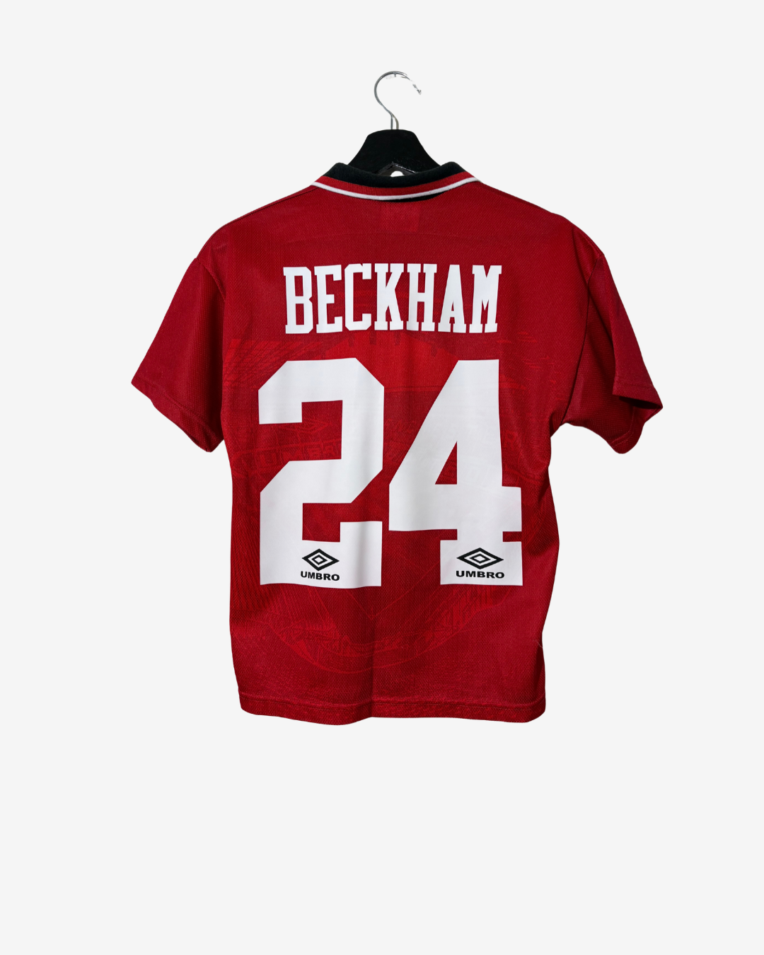 A red short-sleeve football jersey hanging on a black hanger against a light gray background. The back of the shirt features the name 'BECKHAM' and number '24' in white, with Umbro logos below.