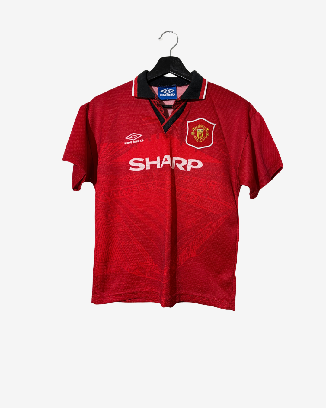 A vintage red Manchester United short-sleeve soccer jersey by Umbro, featuring the white Sharp sponsor logo across the chest, hanging on a black hanger against a light gray background.