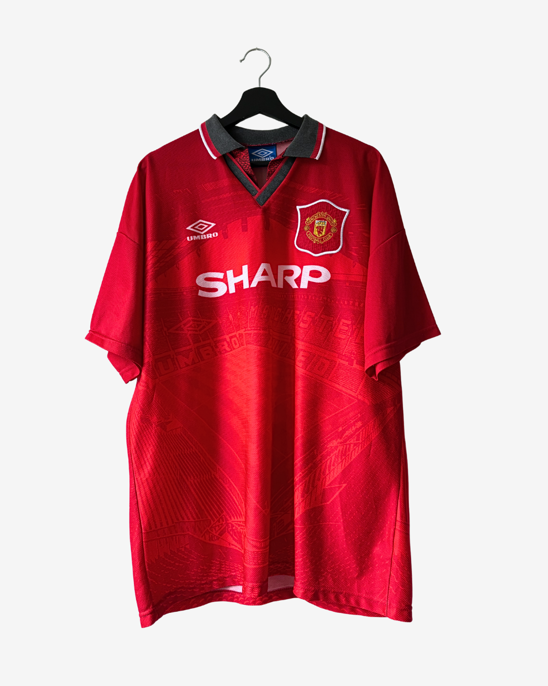 A vintage red Manchester United short-sleeve soccer jersey by Umbro, hanging on a black hanger against a light gray background. The jersey features the Manchester United crest on the left chest, a white SHARP sponsor logo across the center, and the Umbro logo on the right chest.