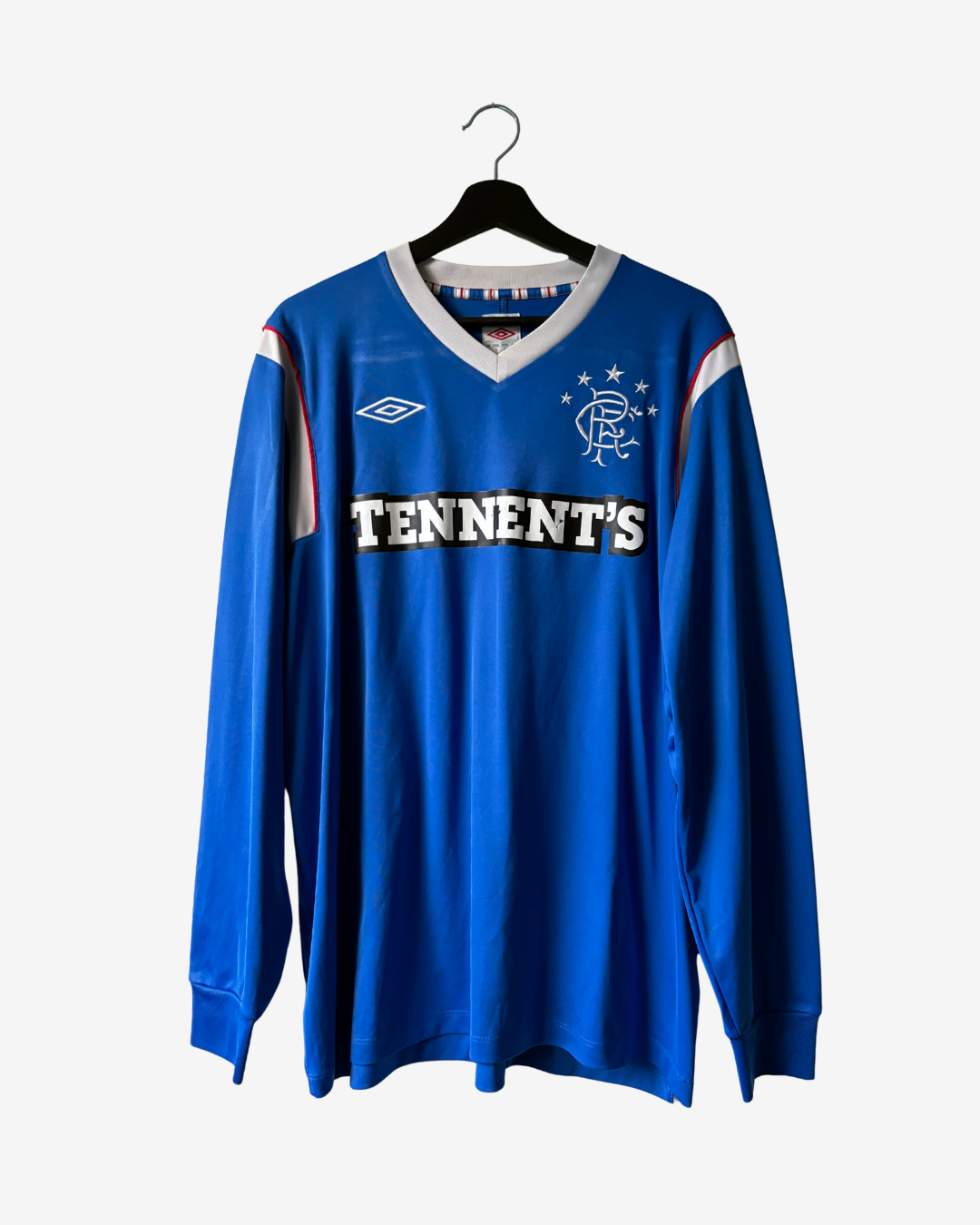 A blue long-sleeve Rangers football jersey with 'TENNENT'S' across the chest, hanging on a black hanger against a light gray background.
