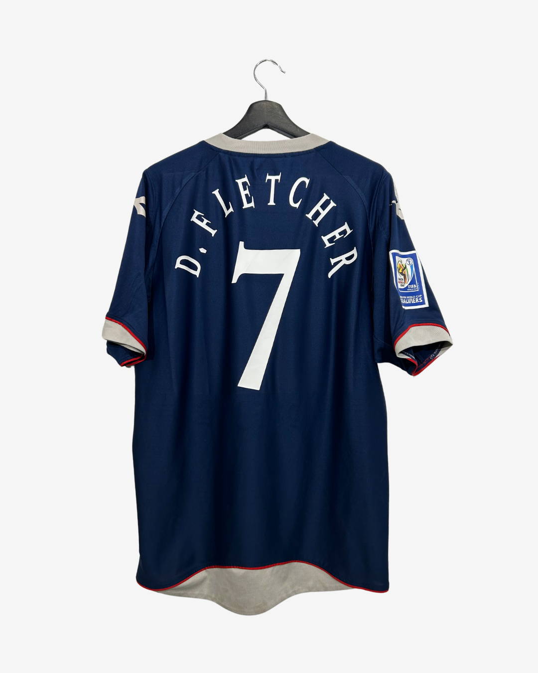 Back view of a navy blue D.Fletcher number 7 soccer jersey hanging on a black hanger against a light gray background.