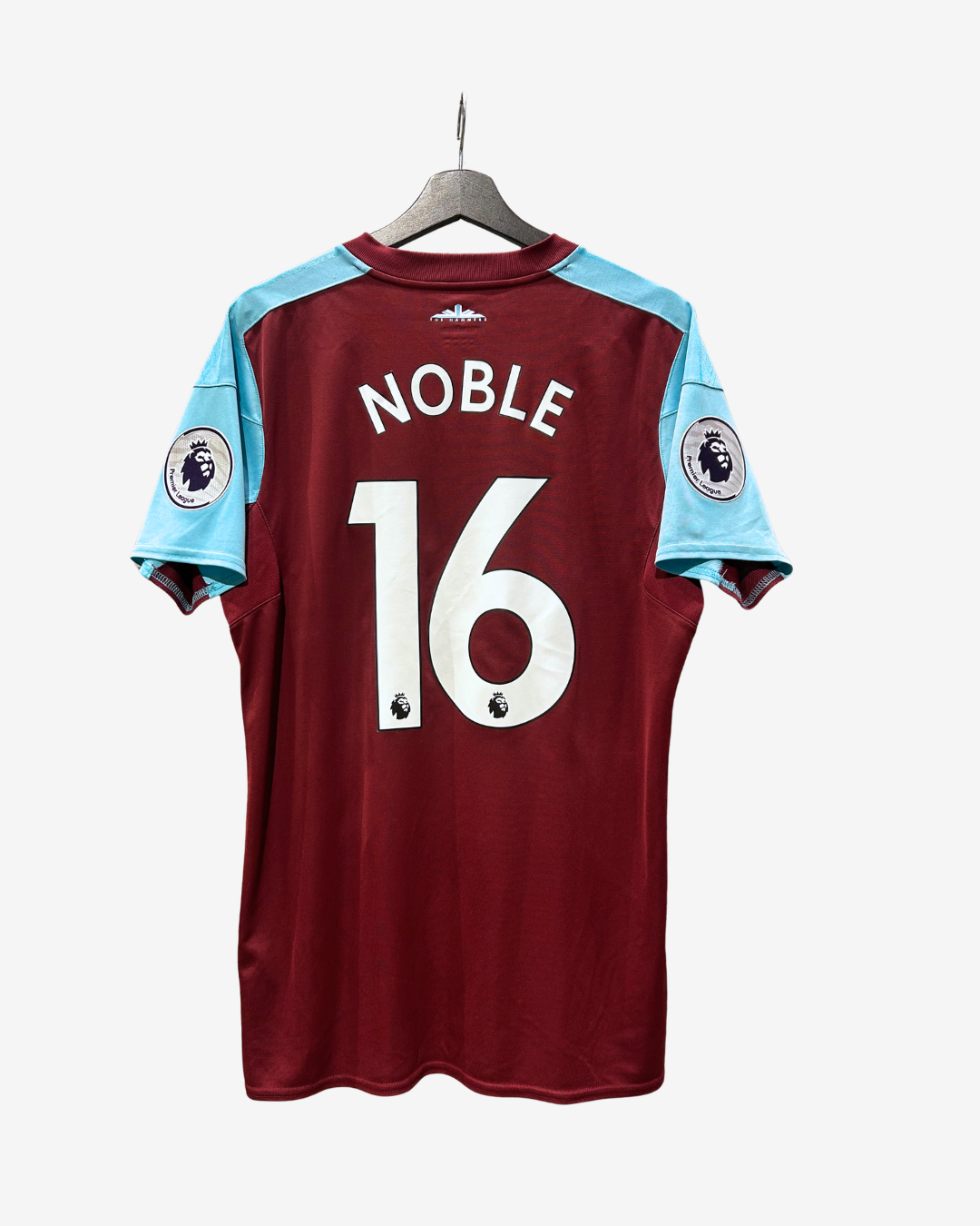 A West Ham United football jersey with 'NOBLE 16' printed on the back, hanging on a wooden hanger against a light gray background.