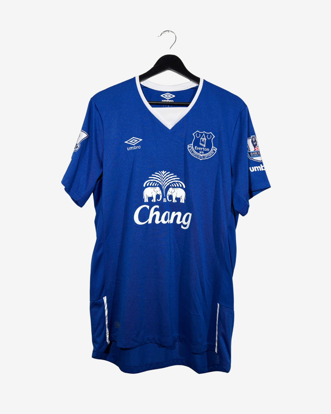 A blue Everton football jersey hanging on a black hanger against a light gray background. The jersey features the white Umbro logo on the right chest, the Everton club crest on the left chest, and the white Chang sponsor logo across the center.